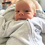 Ronnie is registered to the contest to win money with this photo: baby, child, infant, face, portrait, clothing, gray, blanket, indoor, person, young_child, expression, curious, closeup, soft_texture, casual, unfocused_background, remote_control, shirtless, family