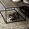 animal, books, cat, cozy, curious, decor, floor, furniture, home, indoor, living_room, metal_legs, patterned_rug, pet, resting, rug, shelf, table, tortoiseshell_cat, wooden_table