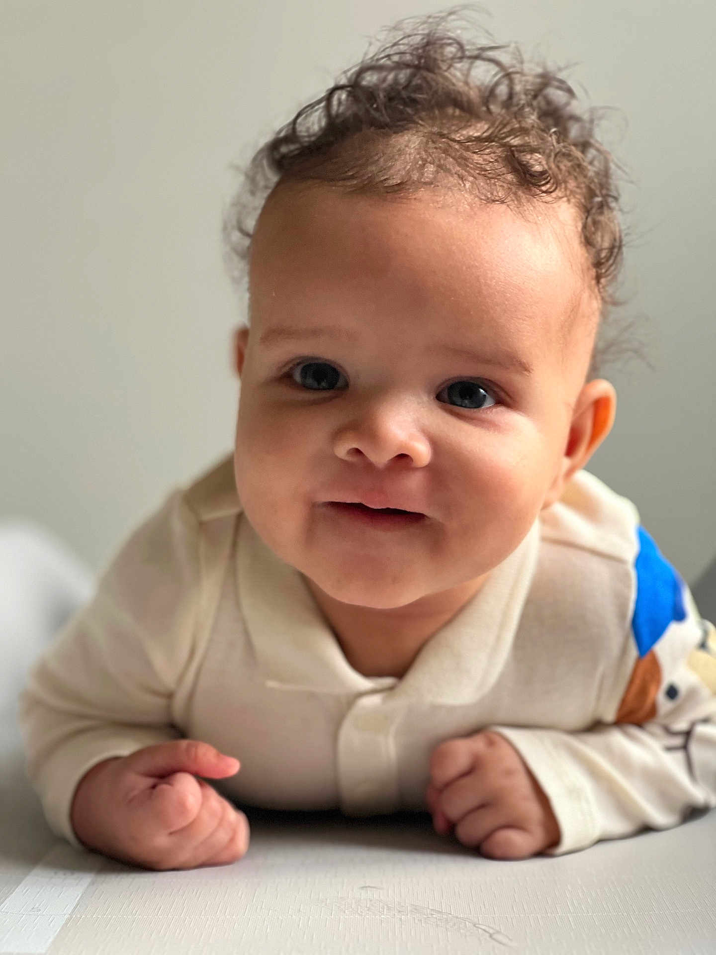 Noah a rejoint le concours — aidez-le/la à gagner de superbes lots ! baby, child, curly_hair, face, hands, light_skin, blue_eyes, clothing, long_sleeves, infant, portrait, propped_up, indoor, cute, closeup, expression, smile, young_child, soft_lighting, white_background