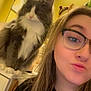 cat, person, glasses, indoor, yellow_wall, mirror, counter, long_hair, black_shirt, fluffy_cat, white_paws, decor, playful_expression, selfie, furniture, home, portrait, pet, cute, casual