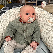 Malone a rejoint le concours — aidez-le/la à gagner de superbes lots ! baby, pacifier, knitwear, cushion, infant, indoor, living_room, mug, television, furniture, cozy, seated, patterned, cute, child, home, soft_lighting, person, casual_clothing, relaxed