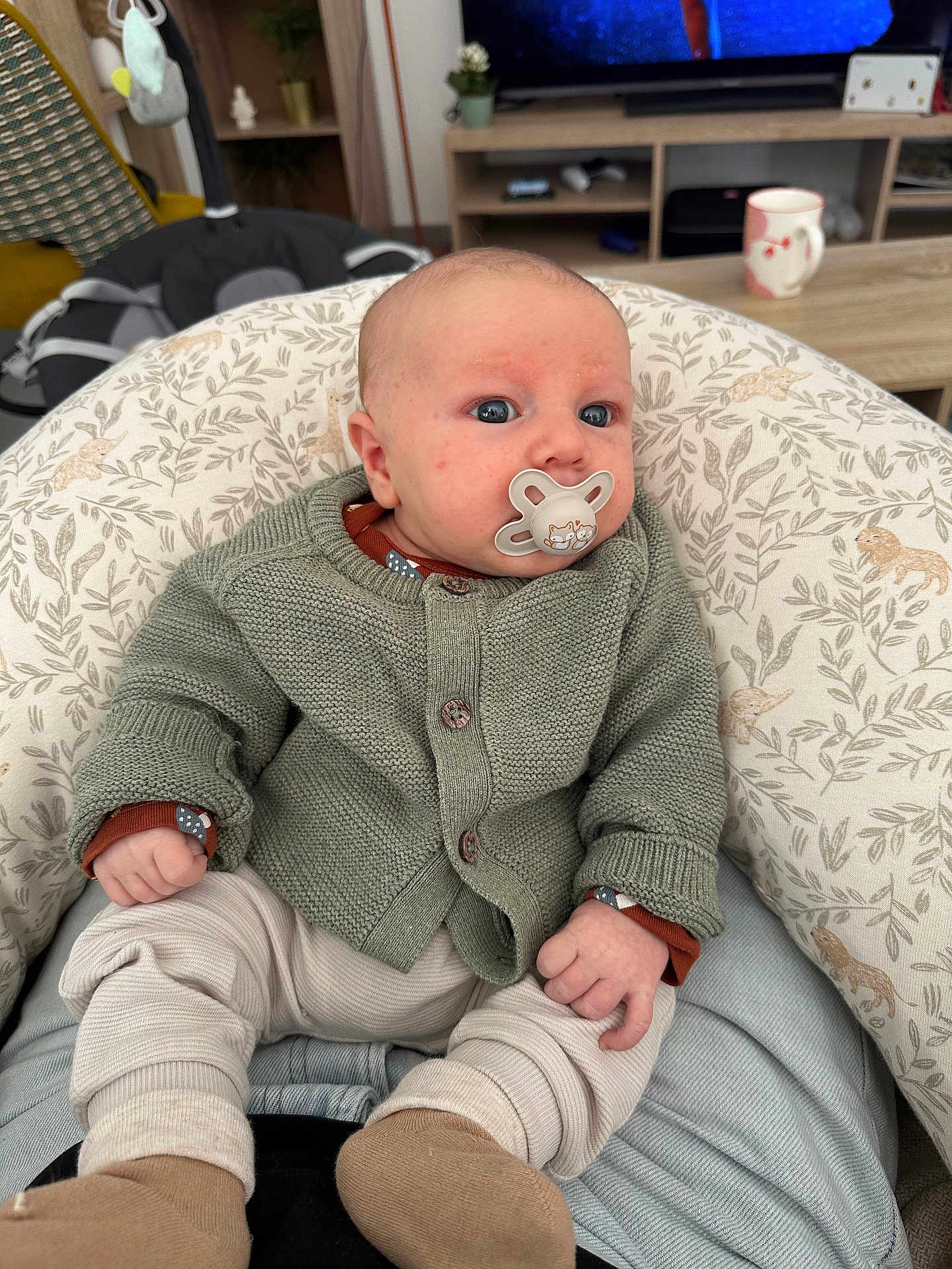 Malone a rejoint le concours — aidez-le/la à gagner de superbes lots ! baby, pacifier, knitwear, cushion, infant, indoor, living_room, mug, television, furniture, cozy, seated, patterned, cute, child, home, soft_lighting, person, casual_clothing, relaxed