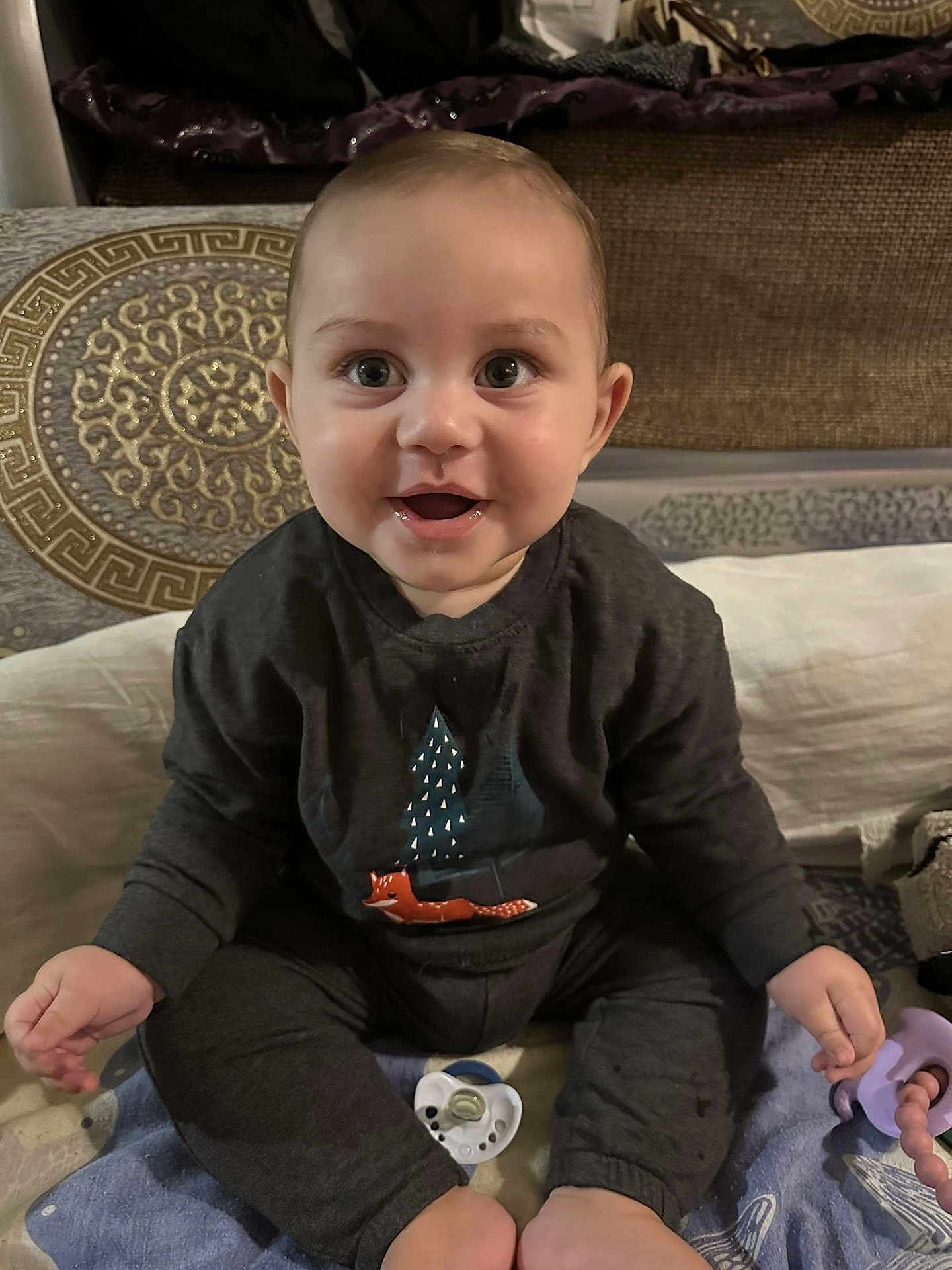 Jalil participe au concours pour gagner de l'argent avec cette photo : baby, child, smiling, sitting, indoors, clothing, toy, pacifier, blanket, bed, cute, face, expression, person, infant, dark_outfit, happy, young, playful, cozy