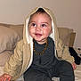 baby, child, smiling, hooded_jacket, necklace, sitting, bed, pillow, plush_toy, indoor, clothing, cute, happy, portrait, infant, sock, cozy, warm, person, young_child
