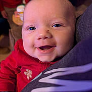Kayce joined the competition — help win amazing prizes! baby, smiling, face, red_clothing, closeup, person, portrait, indoor, happy, child, infant, head, skin, eyes, mouth, warm_lighting, background_blur, comfort, cuddle, expression