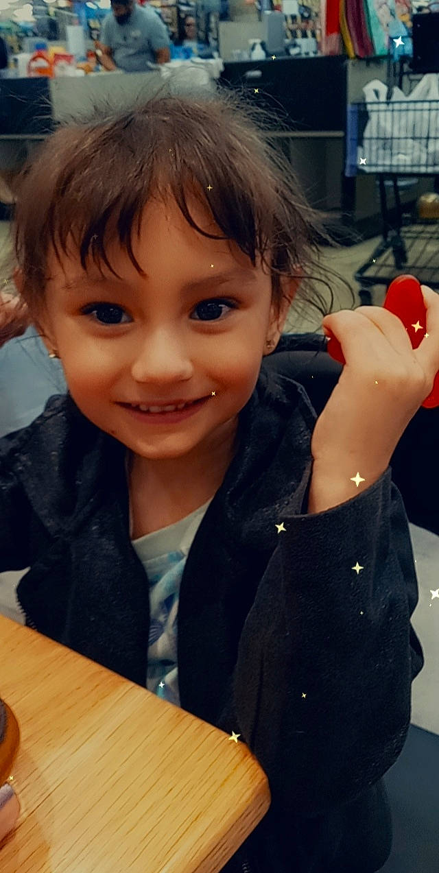 Aiyana is registered to the contest to win money with this photo: bangs, black_hair, chair, cheek, child, event, facial_expression, finger, fun, gesture, happy, joy, nose, person, sitting, skin, smile, t_shirt, table, tableware