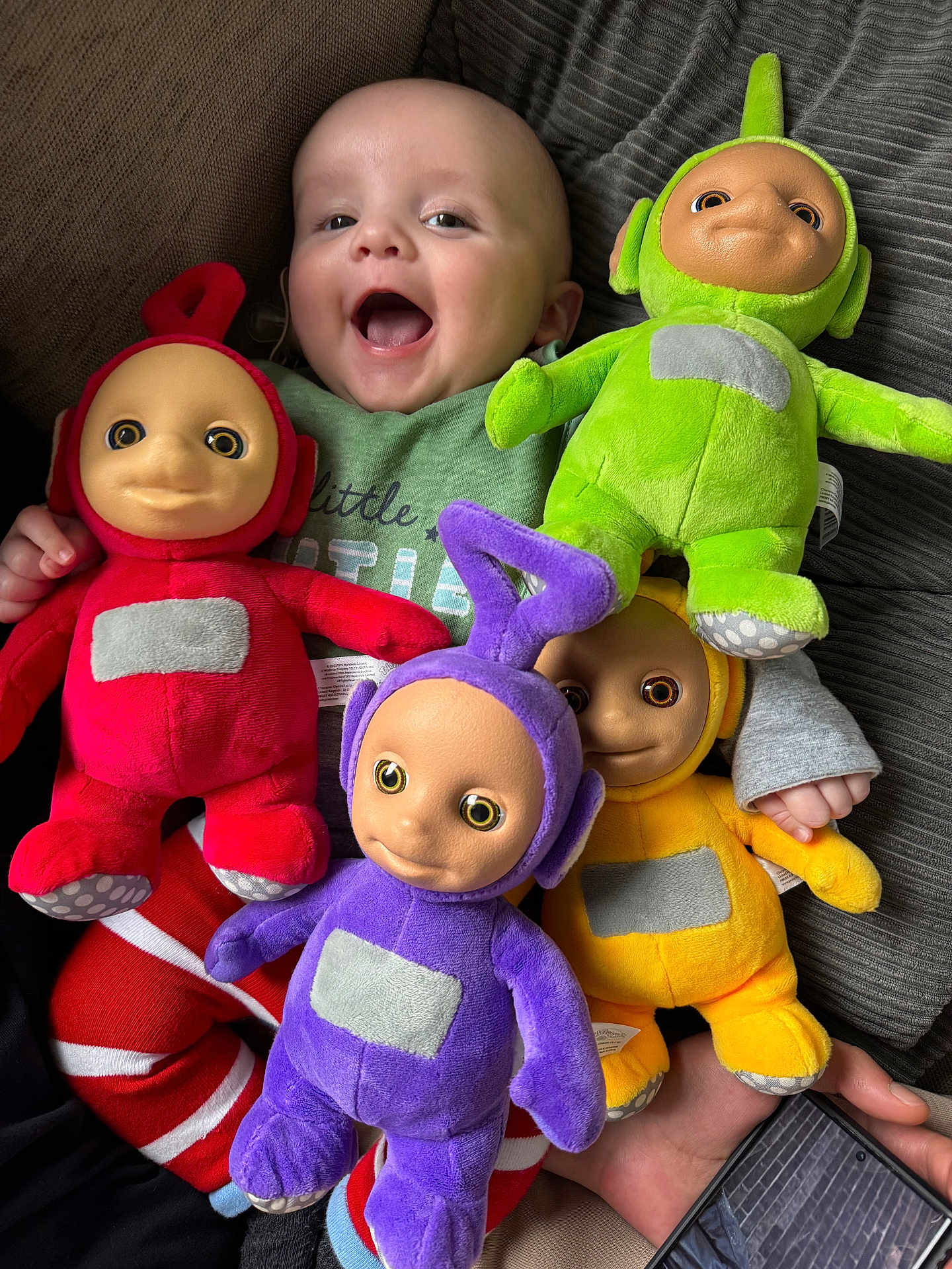 Luchi joined the competition — help win amazing prizes! baby, smiling, laughing, plush_toy, teletubby, red, green, purple, yellow, couch, striped_pants, child, indoor, happy, toy, person, fabric, hand, foot, smartphone