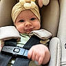 baby, child, car_seat, headband, flower, smile, infant, seatbelt, cute, hand, face, clothing, safety, young_child, indoors, soft_lighting, close_up, happy, person, seat