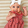 Chloe is registered to the contest to win money with this photo: baby, infant, child, headband, bow, dress, red_stripes, stars, smiling, cute, portrait, lying_down, patterned_blanket, texture, cheeks, skin, eyes, hand, fist, happy