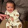Nehemiah is registered to the contest to win money with this photo: baby, child, smiling, pajamas, football_pattern, couch, hand, finger, happy, infant, indoor, person, seated, cute, face, young_child, cozy, fabric, skin, playful