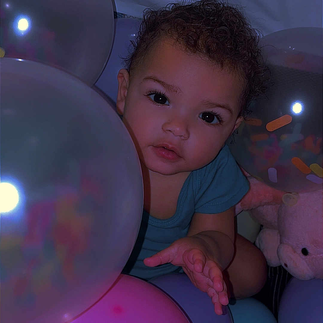 Atyra joined the competition — help win amazing prizes! child, toddler, balloons, curly_hair, plush_toy, indoor, colorful, pastel_colors, baby, cute, expression, portrait, soft_lighting, playful, person, celebration, party, close_up, smiling, curiosity
