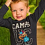 child, boy, smile, blue_eyes, short_hair, long_sleeve_shirt, cartoon_print, outdoor, nature, path, greenery, daylight, happy, cute, portrait, casual_clothing, young, playful, person, forest