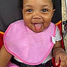 baby, cheeks, child, clothing, cute, eyes, face, hand, happy, indoor, infant, person, pink_bib, pink_pants, portrait, seat, seatbelt, smiling, stroller, tongue_out