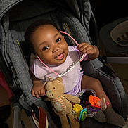 Najiah is registered to the contest to win money with this photo: accessory, baby, car_seat, child, clothing, cute, face, footwear, hand, happy, head, indoor, infant, person, playful, seat, smiling, sunglasses, teddy_bear, toy
