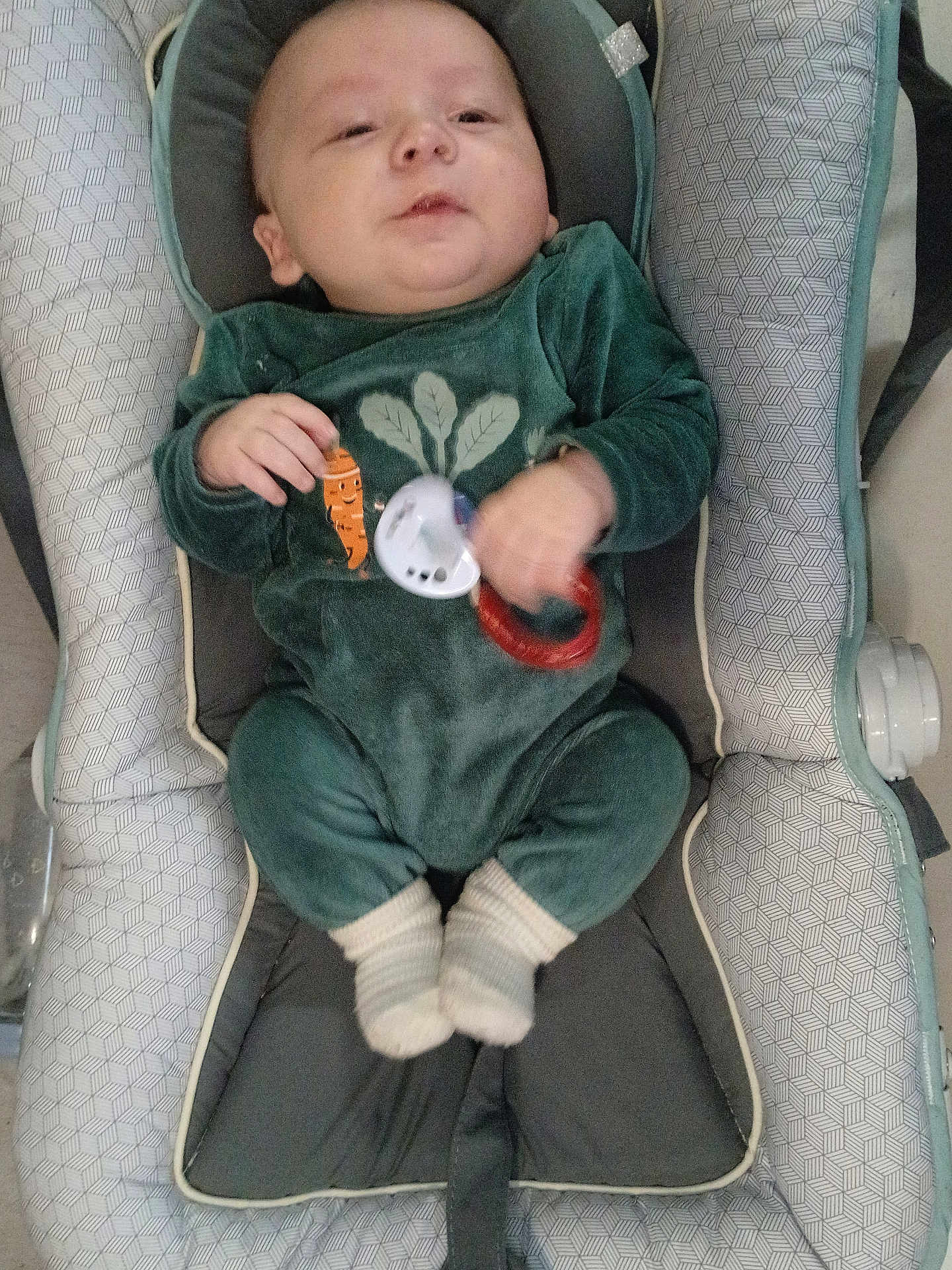 Gabin participe au concours pour gagner de l'argent avec cette photo : baby, infant, car_seat, bouncer, onesie, green_clothing, pacifier, toy_ring, socks, chubby_cheeks, hand, face, head, indoor, fabric_pattern, seat_padding, cozy, portrait, close_up, baby_toys