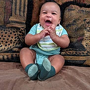 Akeem is registered to the contest to win money with this photo: baby, child, infant, smiling, laughing, sitting, portrait, indoors, couch, cushions, brick_wall, clothing, striped_shirt, shorts, socks, hands, happy, home, cozy, photography