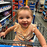Braelynn is registered to the contest to win money with this photo: baby, child, shopping_cart, grocery_store, aisle, snacks, smiling, happy, person, clothing, retail, retail_shelves, store, indoor, food, candy, baby_girl, shopping, cute, infant