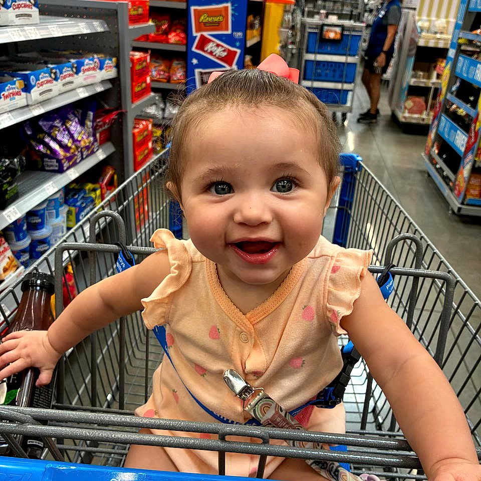 Braelynn is registered to the contest to win money with this photo: baby, child, shopping_cart, grocery_store, aisle, snacks, smiling, happy, person, clothing, retail, retail_shelves, store, indoor, food, candy, baby_girl, shopping, cute, infant