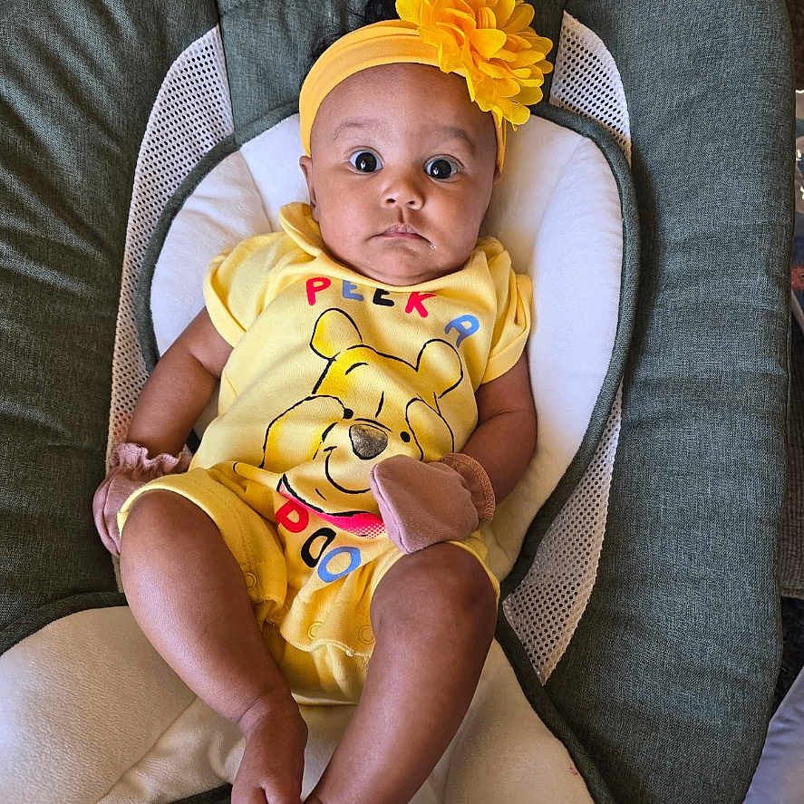 Aria is registered to the contest to win money with this photo: baby, baby_chair, bright_colors, child, comfortable, cushion, cute, flower, headband, indoors, infant, looking_at_camera, mittens, person, portrait, sitting, soft_toys, winnie_the_pooh, yellow_clothing, young_child
