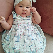 Miah is registered to the contest to win money with this photo: baby, infant, child, headband, bow, dress, sailboat_pattern, white_tights, pillow, couch, soft_fabric, indoors, cute, adorable, chubby_cheeks, relaxed, portrait, person, sleepwear, resting