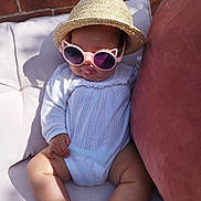 Miah is registered to the contest to win money with this photo: baby, brick_wall, child, couch, cute, drool, fashion, hand, hat, infant, legs, outdoor, pillow, portrait, relaxing, shadow, straw_hat, sunglasses, sunlight, white_clothing