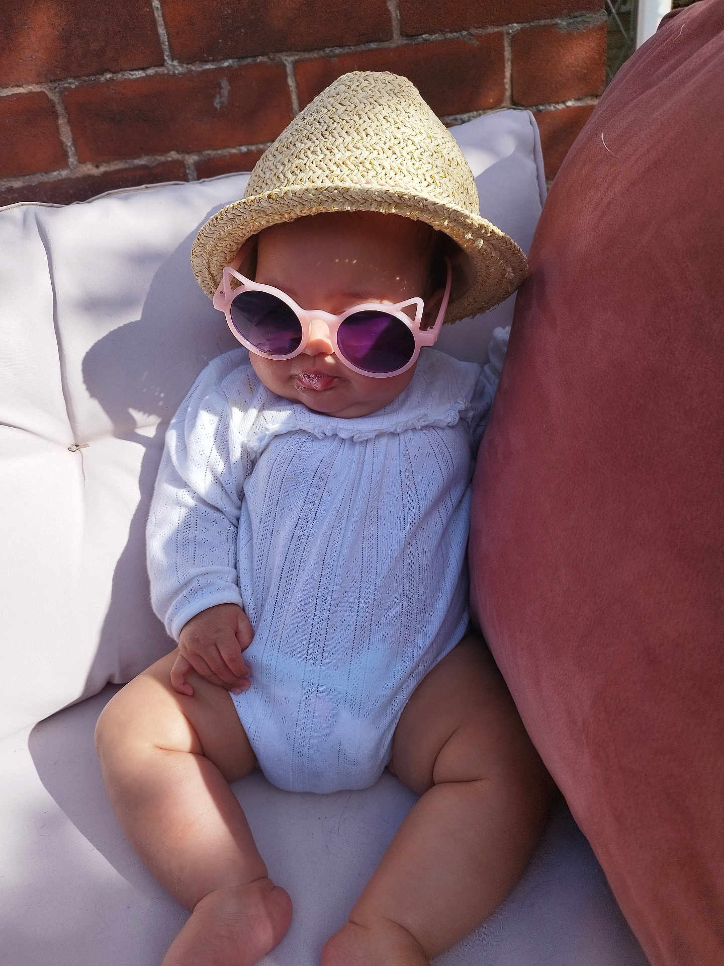 Miah is registered to the contest to win money with this photo: baby, brick_wall, child, couch, cute, drool, fashion, hand, hat, infant, legs, outdoor, pillow, portrait, relaxing, shadow, straw_hat, sunglasses, sunlight, white_clothing