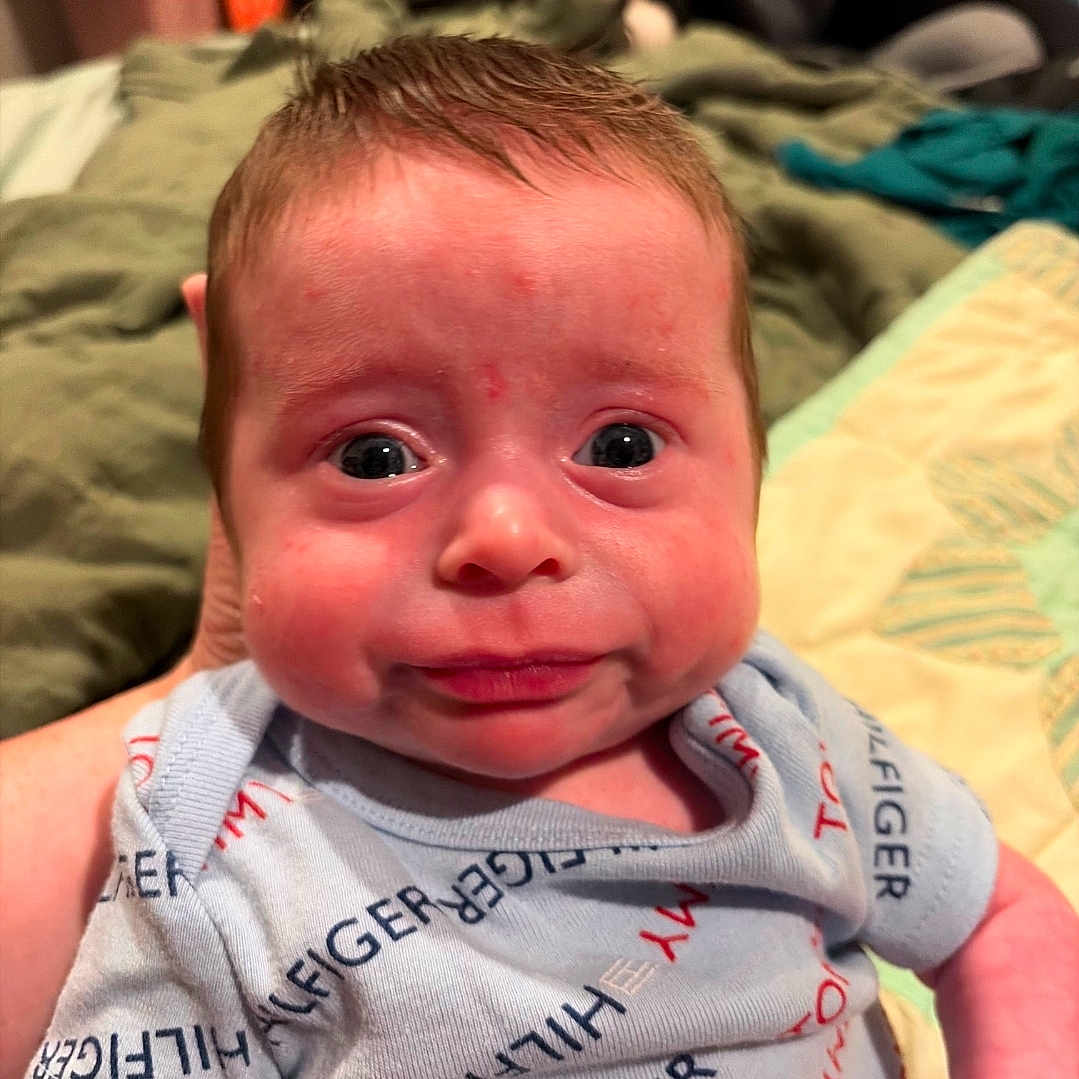 Wyatt is registered to the contest to win money with this photo: baby, infant, face, expression, clothing, onesie, blue, person, newborn, wide_eyes, indoor, holding, blanket, car_seat, cute, skin, portrait, child, human, sleepwear
