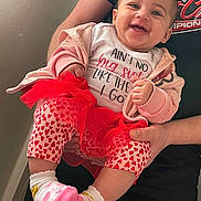 Deaira joined the competition — help win amazing prizes! baby, child, smiling, pink_clothing, heart_pattern, socks, hoodie, toddler, person, holding, hands, indoor, wall, shirt, text, happy, cute, portrait, family, infant