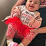 baby, child, smiling, pink_clothing, heart_pattern, socks, hoodie, toddler, person, holding, hands, indoor, wall, shirt, text, happy, cute, portrait, family, infant