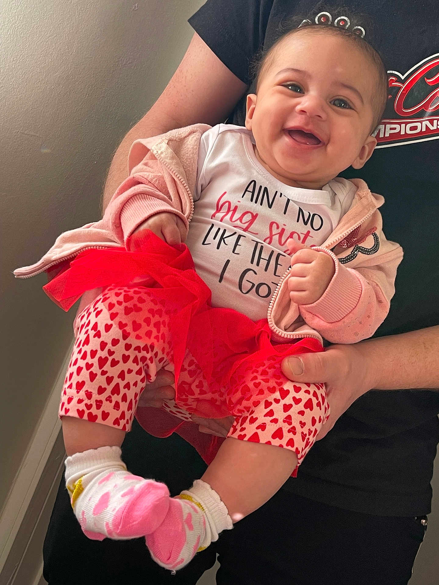 Deaira joined the competition — help win amazing prizes! baby, child, smiling, pink_clothing, heart_pattern, socks, hoodie, toddler, person, holding, hands, indoor, wall, shirt, text, happy, cute, portrait, family, infant