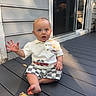 baby, child, outdoor, deck, wood, shirt, shorts, waving, expression, sunlight, shadow, house, window, door, plank, sitting, person, cute, summer, casual