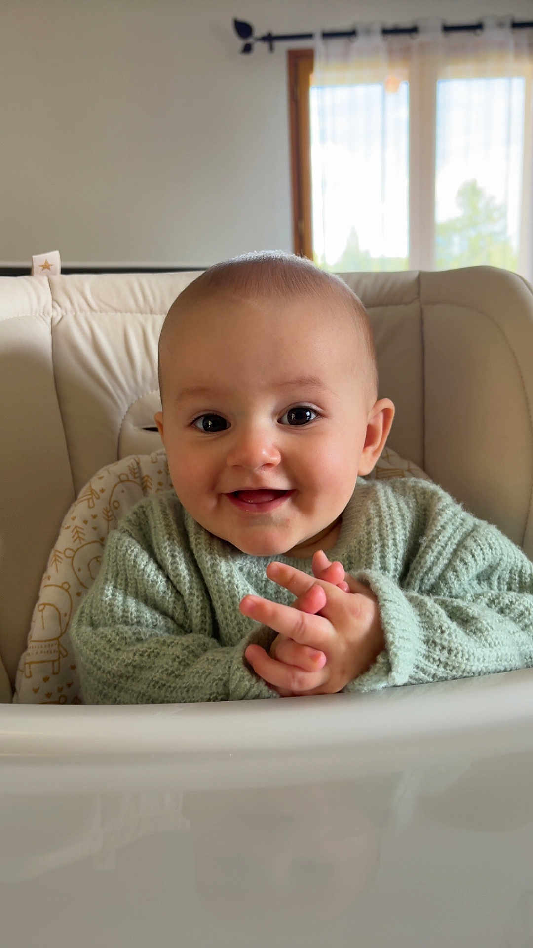 Agathe participe au concours pour gagner de l'argent avec cette photo : baby, child, high_chair, sweater, smiling, hands, face, indoor, window, curtain, light, infant, person, cute, knitwear, happy, portrait, seated, skin, eyebrows