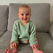 Agathe participe au concours pour gagner de l'argent avec cette photo : baby, child, smiling, sitting, couch, sweater, knitted, green_sweater, barefoot, hands, feet, indoor, living_room, happy, cute, portrait, face, person, young_child, cozy