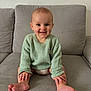 baby, child, smiling, sitting, couch, sweater, knitted, green_sweater, barefoot, hands, feet, indoor, living_room, happy, cute, portrait, face, person, young_child, cozy