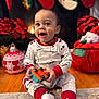 Nasir joined the competition — help win amazing prizes! baby, child, toy, pajamas, smiling, holiday, christmas_stockings, poinsettia, fireplace, floor, carpet, indoor, festive, decorations, red, white, green, cute, happy, person