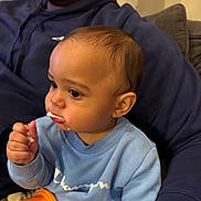 Nasir is registered to the contest to win money with this photo: baby, child, person, sitting, indoor, food, snack, cup, blue_sweatshirt, adult, lap, beard, hoodie, orange_cup, crumbs, face, hand, closeup, casual, cozy