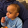 baby, child, person, sitting, indoor, food, snack, cup, blue_sweatshirt, adult, lap, beard, hoodie, orange_cup, crumbs, face, hand, closeup, casual, cozy