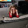cartoon, child, computer_chair, cookie, couch, curious, decor, expression, face, furniture, girl, home, indoor, living_room, person, photography, red_shirt, shelf, television, toy