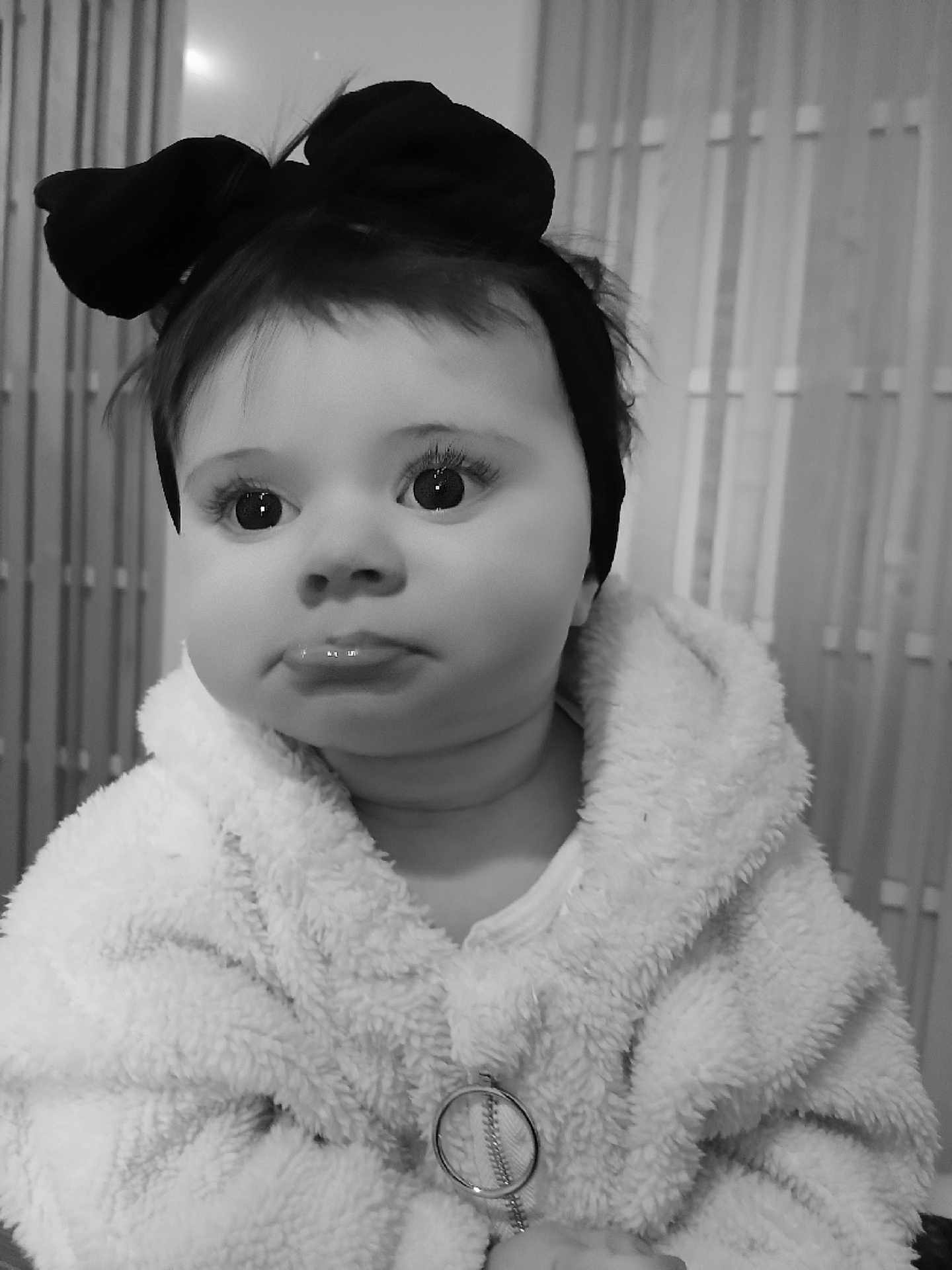 Délia C participe au concours pour gagner de l'argent avec cette photo : baby, child, portrait, black_and_white, headband, bow, fluffy_jacket, cute, expression, face, indoor, soft_texture, young, person, close_up, warm_clothing, adorable, infant, looking_away, monochrome
