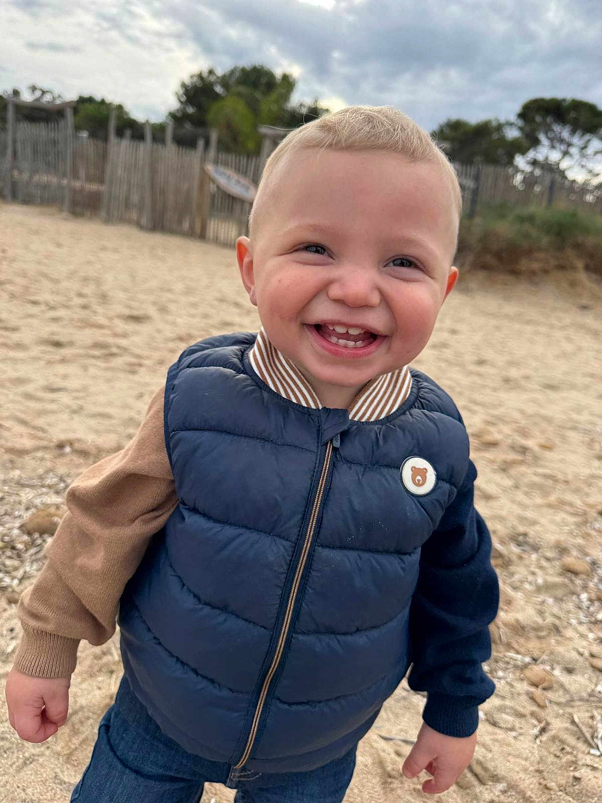 Ewen participe au concours pour gagner de l'argent avec cette photo : toddler, child, smiling, outdoor, beach, sand, vest, clothing, happy, portrait, casual, cute, boy, face, person, nature, daylight, fence, sky, jackets
