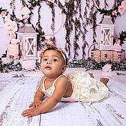 Ayla is registered to the contest to win money with this photo: baby, child, infant, dress, flower_headband, floor, wooden_floor, lantern, pink_roses, greenery, floral, laying_down, cute, portrait, decor, vintage, background, innocent, happy, studio_photo