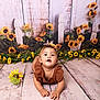 Ayla is registered to the contest to win money with this photo: baby, child, toddler, sunflower, flower, headband, brown_clothing, wooden_floor, rustic, picket_fence, greenery, indoor, portrait, cute, curious, flooring, plant, nature, background, studio
