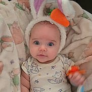 Harpy is registered to the contest to win money with this photo: baby, infant, bunny_ears, costume, carrot, blanket, toy, cute, child, person, indoors, soft, plush, sleepwear, patterned_clothing, headgear, wide_eyes, sitting, small_hands, looking_up