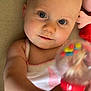 baby, infant, child, face, blue_eyes, rattle, toy, plush_toy, white_tank_top, pink_clothing, close_up, skin, arm, hand, lying_down, curious, indoors, soft_toy, playful, portrait