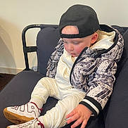 Enzo a rejoint le concours — aidez-le/la à gagner de superbes lots ! toddler, child, sitting, couch, jacket, sneakers, cap, white_clothing, black_cap, indoor, furniture, young_child, casual, footwear, cozy, person, portrait, cute, fashion, relaxed