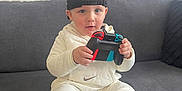 Enzo a rejoint le concours — aidez-le/la à gagner de superbes lots ! toddler, child, sitting, couch, controller, video_game, cap, white_clothing, sneakers, indoor, person, gaming, casual, footwear, hoodie, cute, focused, modern, living_room, playful