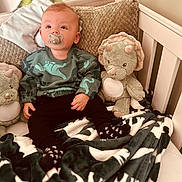 Daemon is registered to the contest to win money with this photo: baby, pacifier, dinosaur, plush_toy, blanket, crib, pillow, sweater, child, infant, stuffed_animal, nursery, furniture, soft_toy, cozy, indoors, cute, smiling, person, comfortable