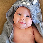 Ella participe au concours pour gagner de l'argent avec cette photo : baby, infant, smile, face, hooded_towel, gray_towel, cute, skin, cheeks, child, soft_texture, blanket, lying_down, indoors, portrait, young, cozy, warm, happy, wrapped