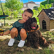 Gabriel a rejoint le concours — aidez-le/la à gagner de superbes lots ! boy, child, dog, pet, outdoor, garden, tree, grass, doghouse, crouching, toy, sunlight, happy, smiling, greenery, nature, cushion, baby_hand, play, casual_clothing
