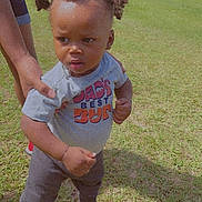 Clifford is registered to the contest to win money with this photo: baby, bodypart, clothing, face, finger, footwear, grass, hand, head, lawn, outdoors, pants, people, person, photography, plant, portrait, shoe, shorts, t_shirt